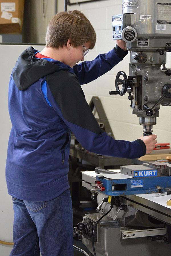 CRAFT - Working on the mill, sophomore Lewis Yeich drills holes in a piece of wood. Everything the machine shop students worked on was a hands-on activity. “We made different tools such as hammers, wrenches, and many other things made of metal,” Yeich said.