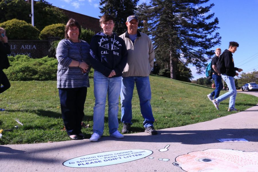 Sophomore Kevin Devine with his parents, Kelly and Patrick Devine, standing next to the finished storm drain painting.