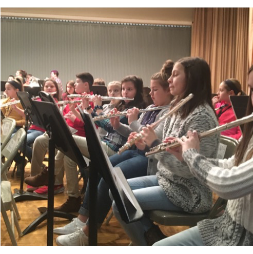 In a photo from before the pandemic, flute players read music and pay attention to the directors during a symphonic band rehearsal. 
